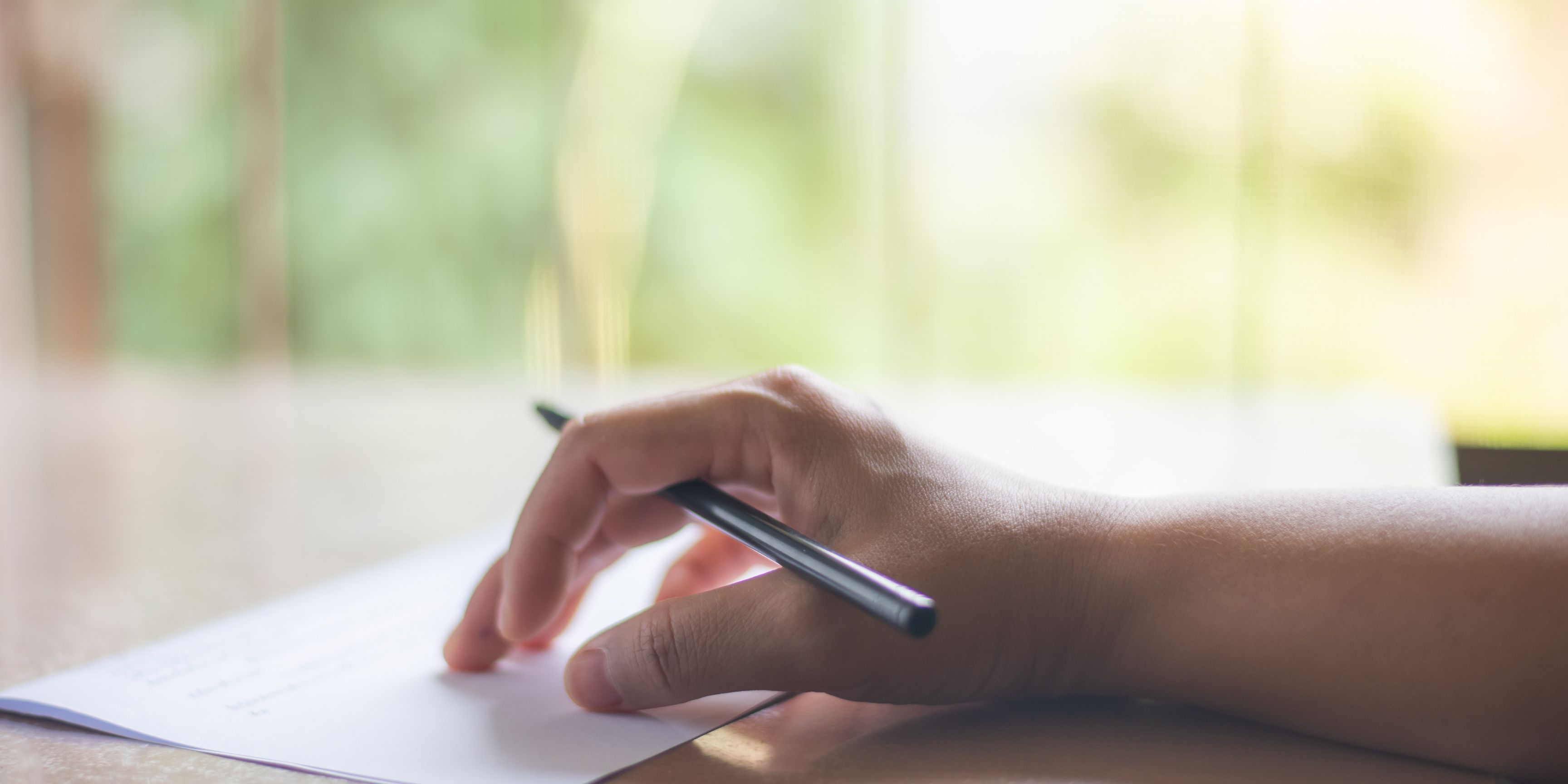 a hand holds a pen above a piece of paper writing a letter