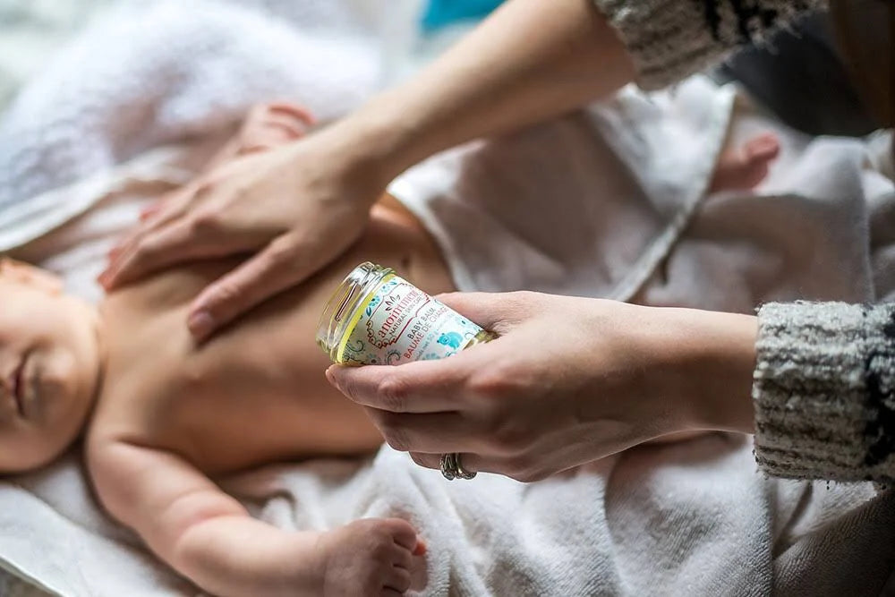 postpartum essentails from the tare shop. a hand rubs baby balm onto a newborn