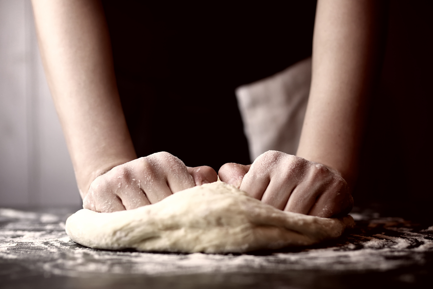 making your own pizza dough is so easy! two hands knead dough on a floured surface