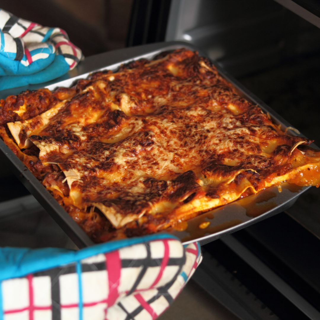 a zero waste lasagna is getting pulled out of the oven by someone wearing white, red, and blue oven mitts.