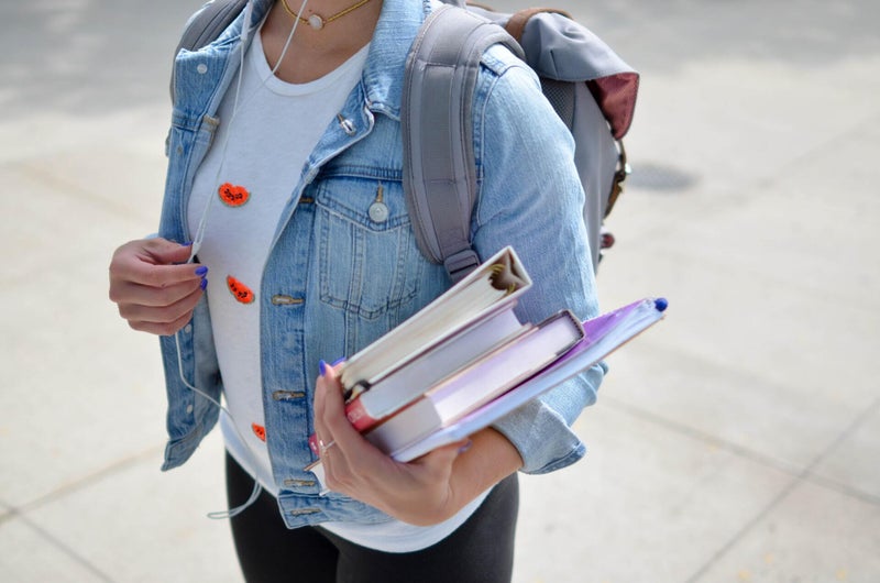 A woman holds books and a binder wearing a backpack