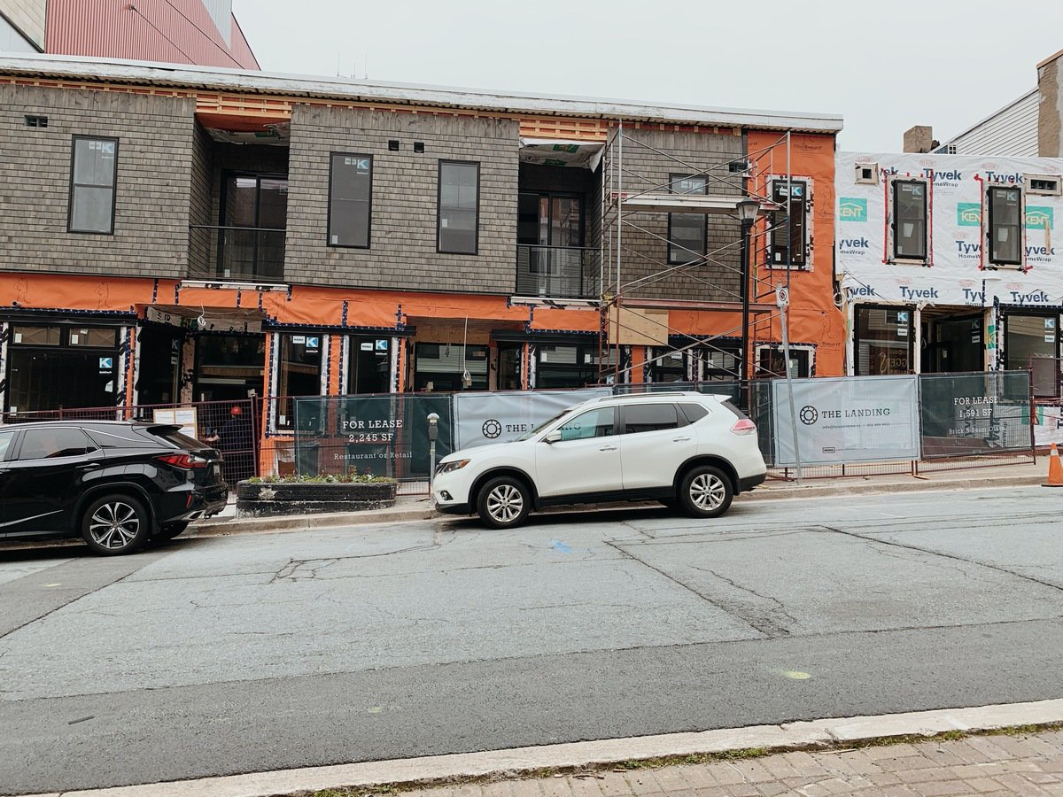 The Dartmouth Tare Shop is covered in scaffolding and construction materials with cars parked on the street in front of it. 