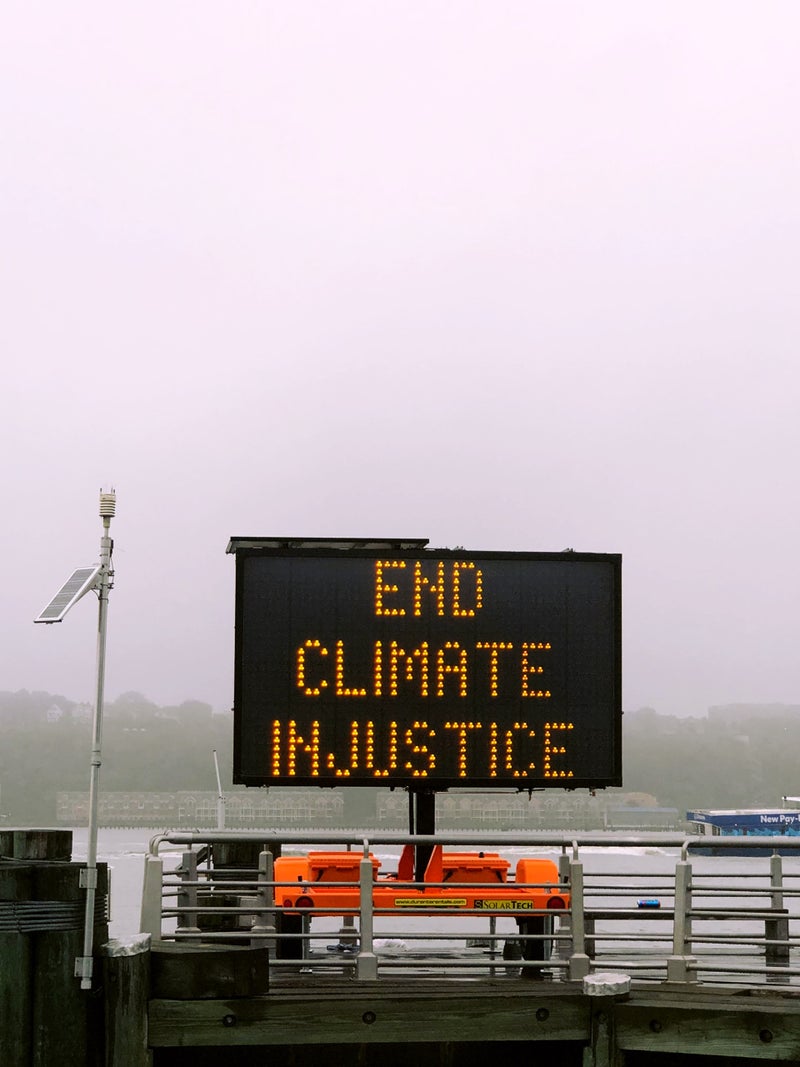 A road work sign that reads "End Climate Justice" sits by the water