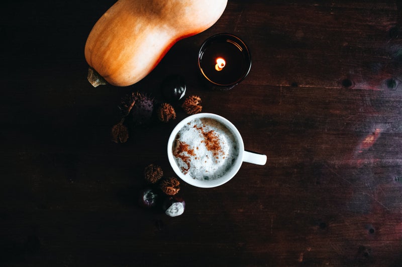 A cup of pumpkin spiced latte sits with a butternut squash on a wooden table.