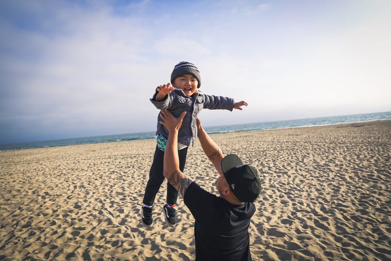 A boy is playfully thrown up in the air by his father at the beach