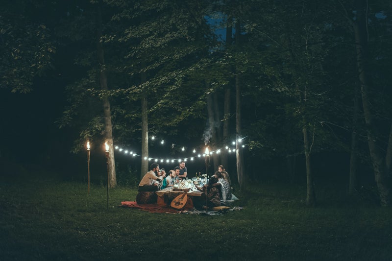 a family sits on blankets in the forest with string lights around them