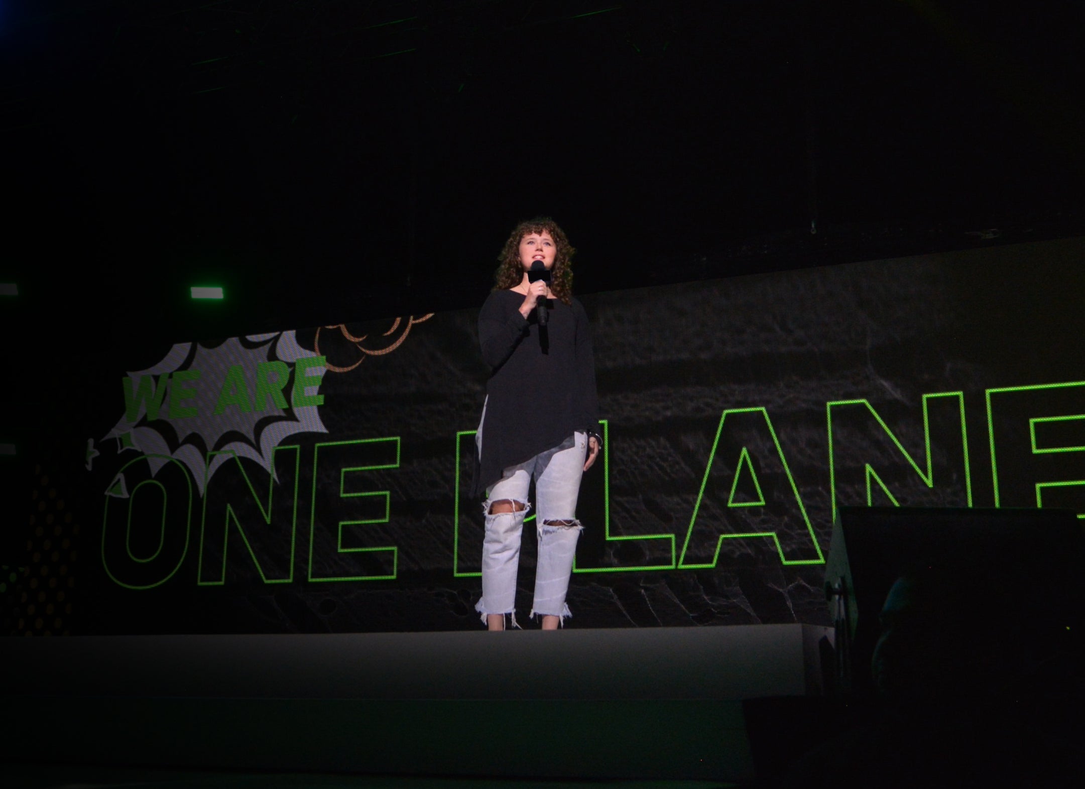 Kate Pepler stands on a stage holding a microphone speaking to the audience.