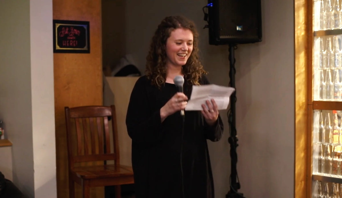 Kate Pepler smiles holding a microphone and reading from a paper