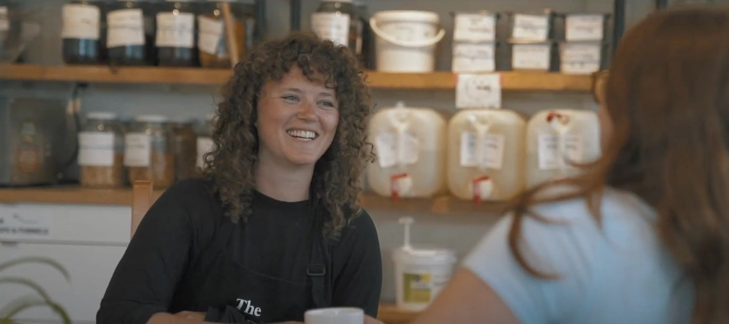 Kate Pepler smiles, sitting at a cafe table speaking to someone